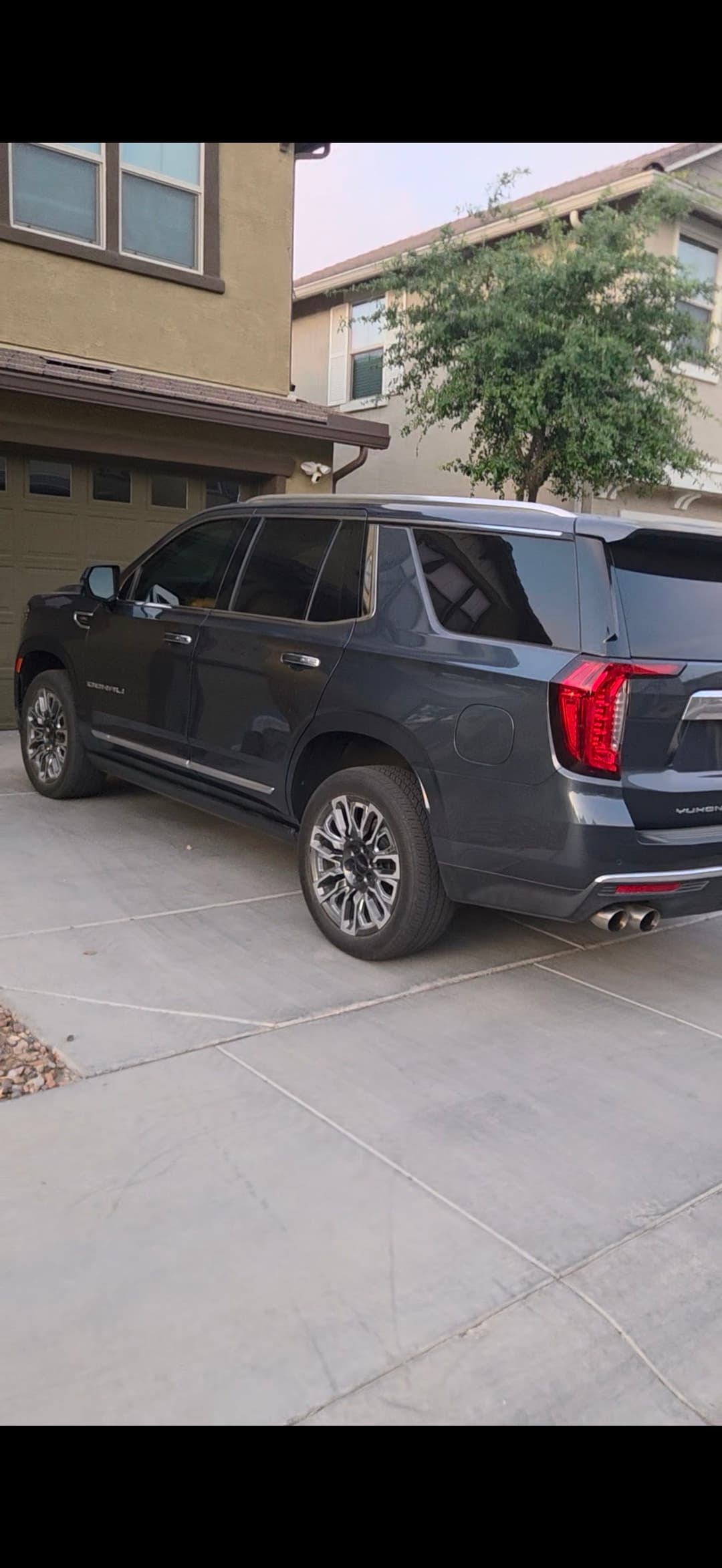 Dark gray SUV parked in a driveway of a suburban home with greenery nearby.