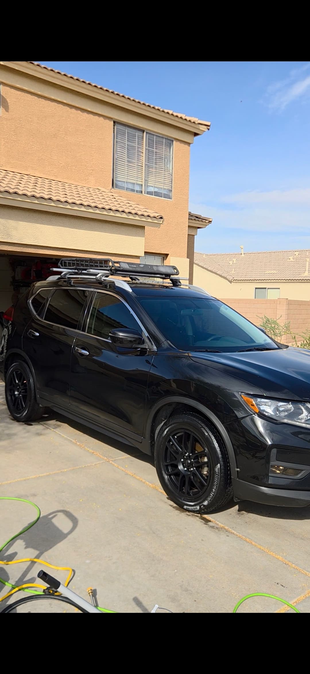 Black SUV parked in driveway with roof rack, modern home in background.