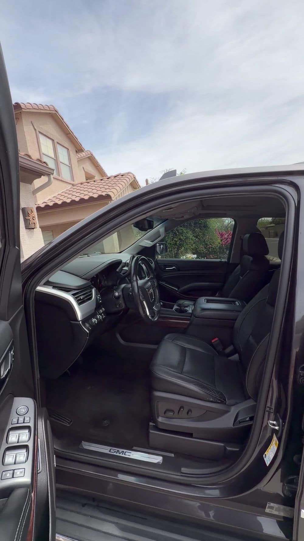Interior view of a black SUV parked outside a house, showcasing leather seats and dashboard.