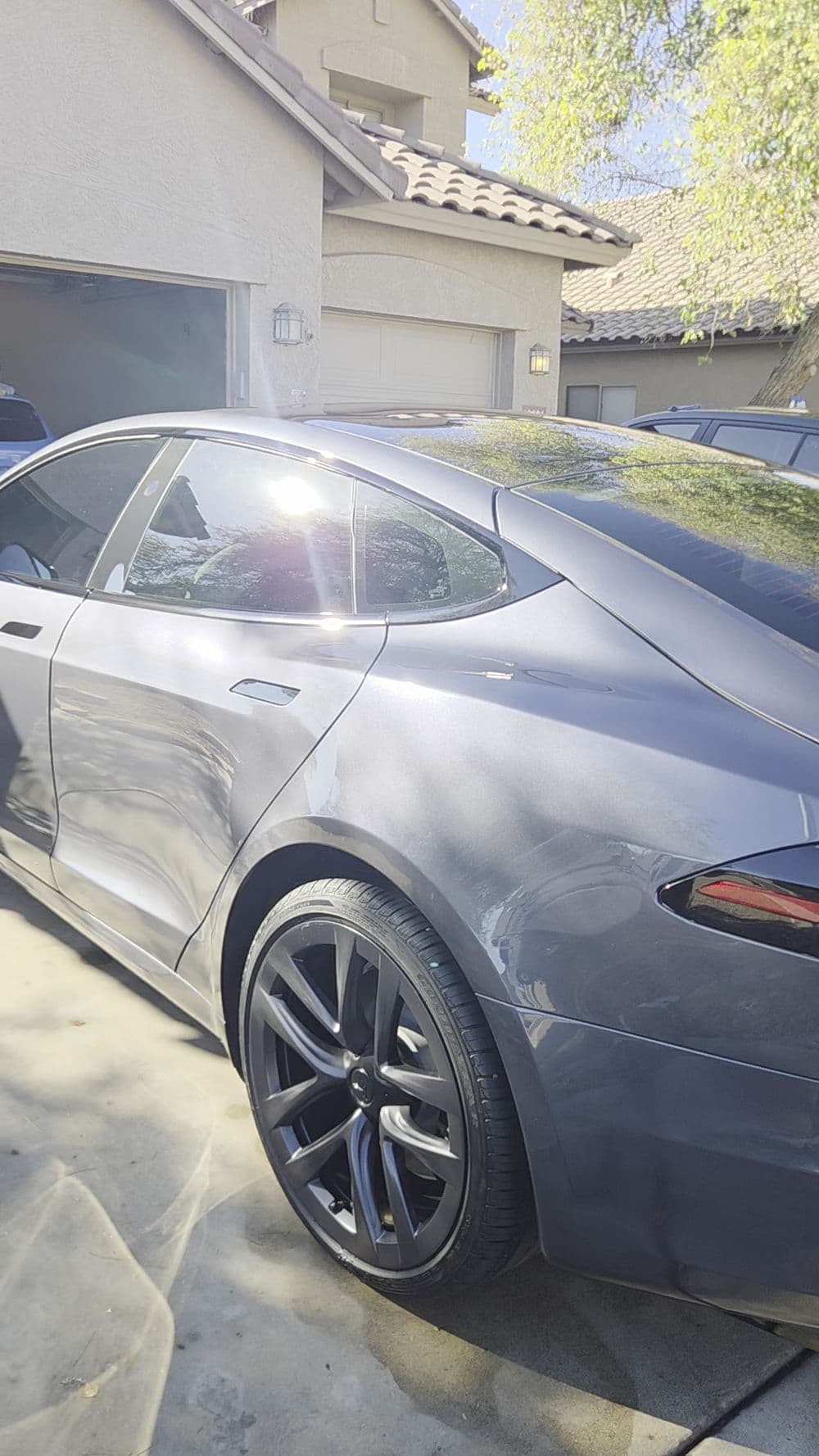 Gray sports car parked in driveway with sunlight reflecting on sleek surface.