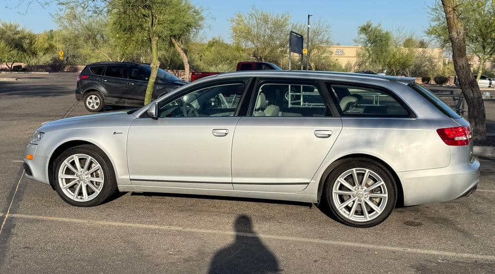 Silver Audi wagon parked in a desert landscape with sparse vegetation and distant buildings.