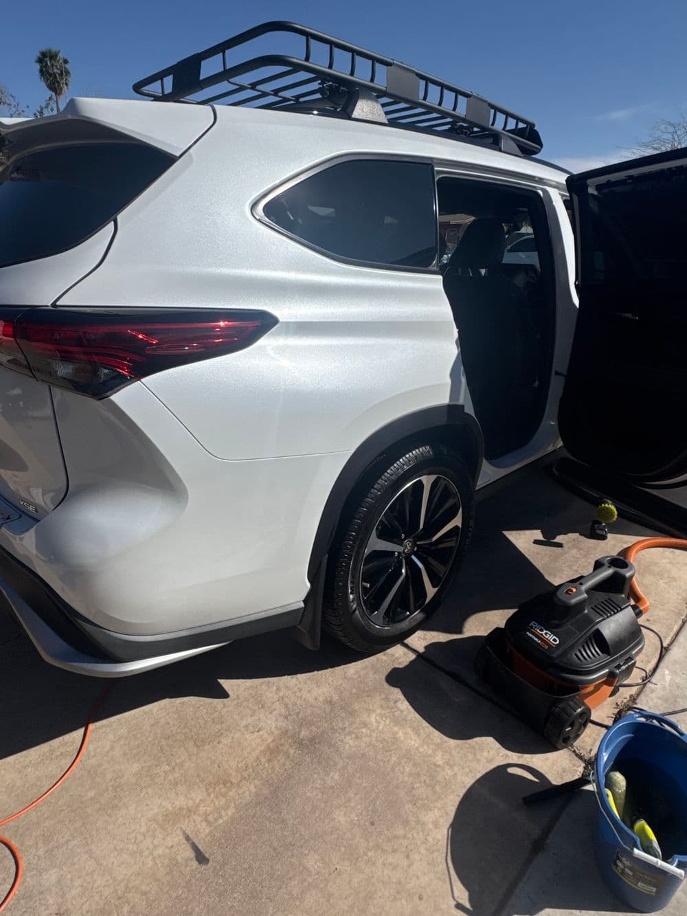 White SUV with roof rack, parked outdoors next to a vacuum and bucket for cleaning.