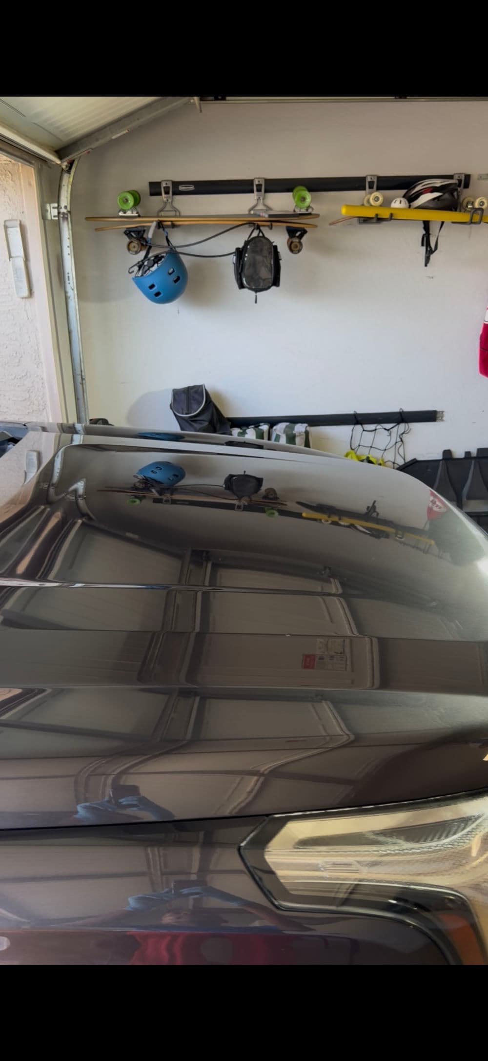 Shiny car hood reflecting garage tools and gear in organized space.