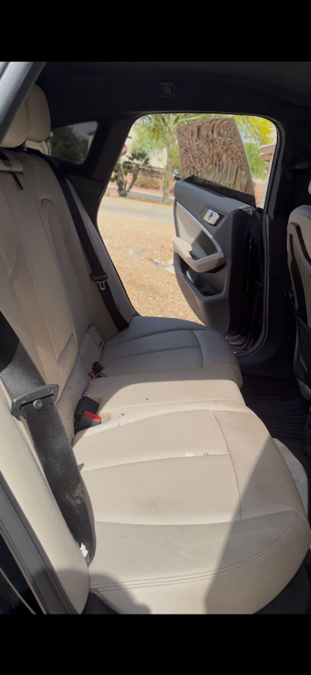 Interior view of a car's backseat, featuring beige upholstery and an open door.
