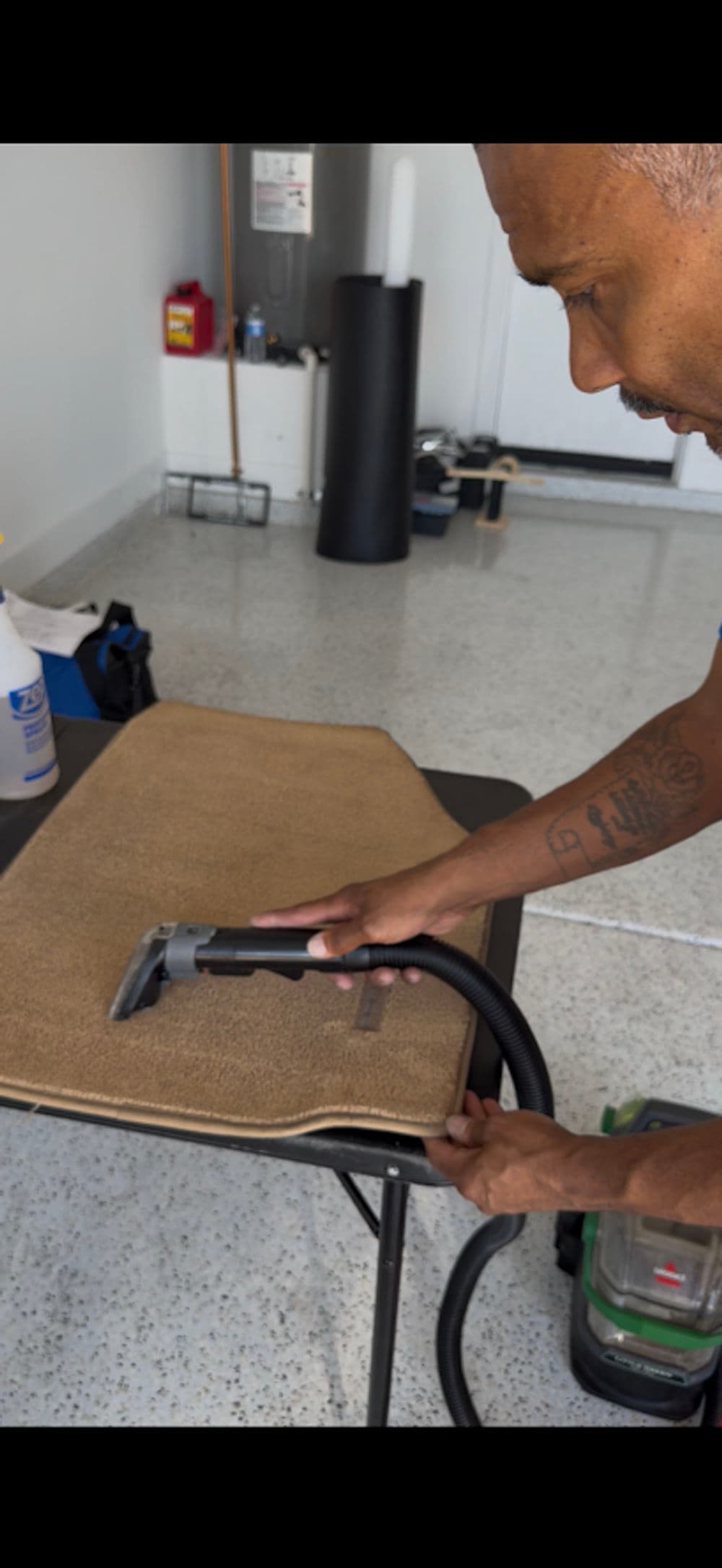 Person using a vacuum cleaner on a carpeted surface in a well-lit room.