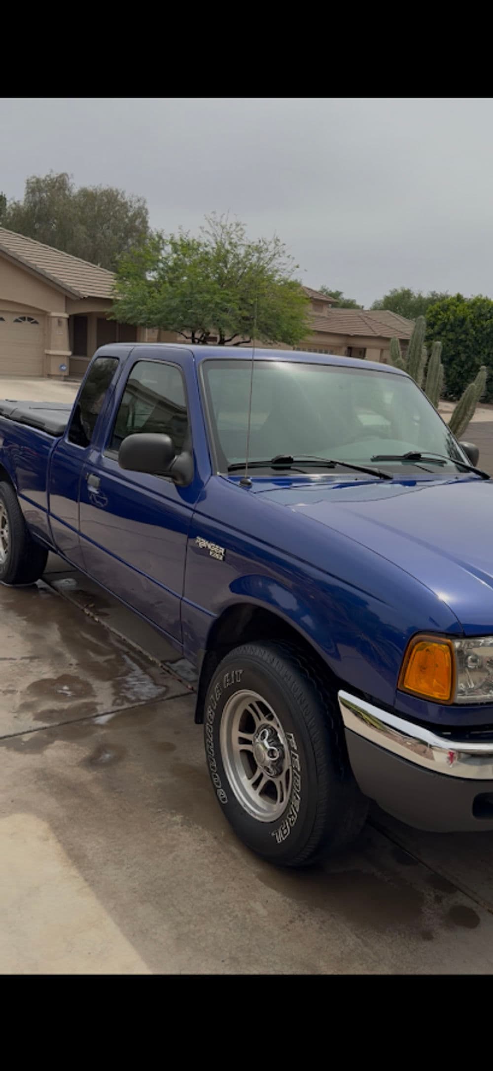 Blue pickup truck parked in a residential driveway with clear sky and greenery.