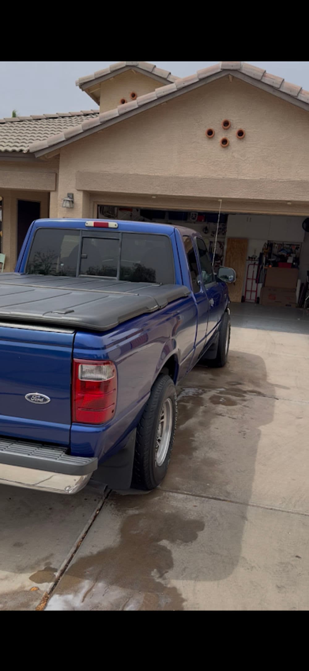 Blue pickup truck parked in driveway in front of a garage with cluttered interior.