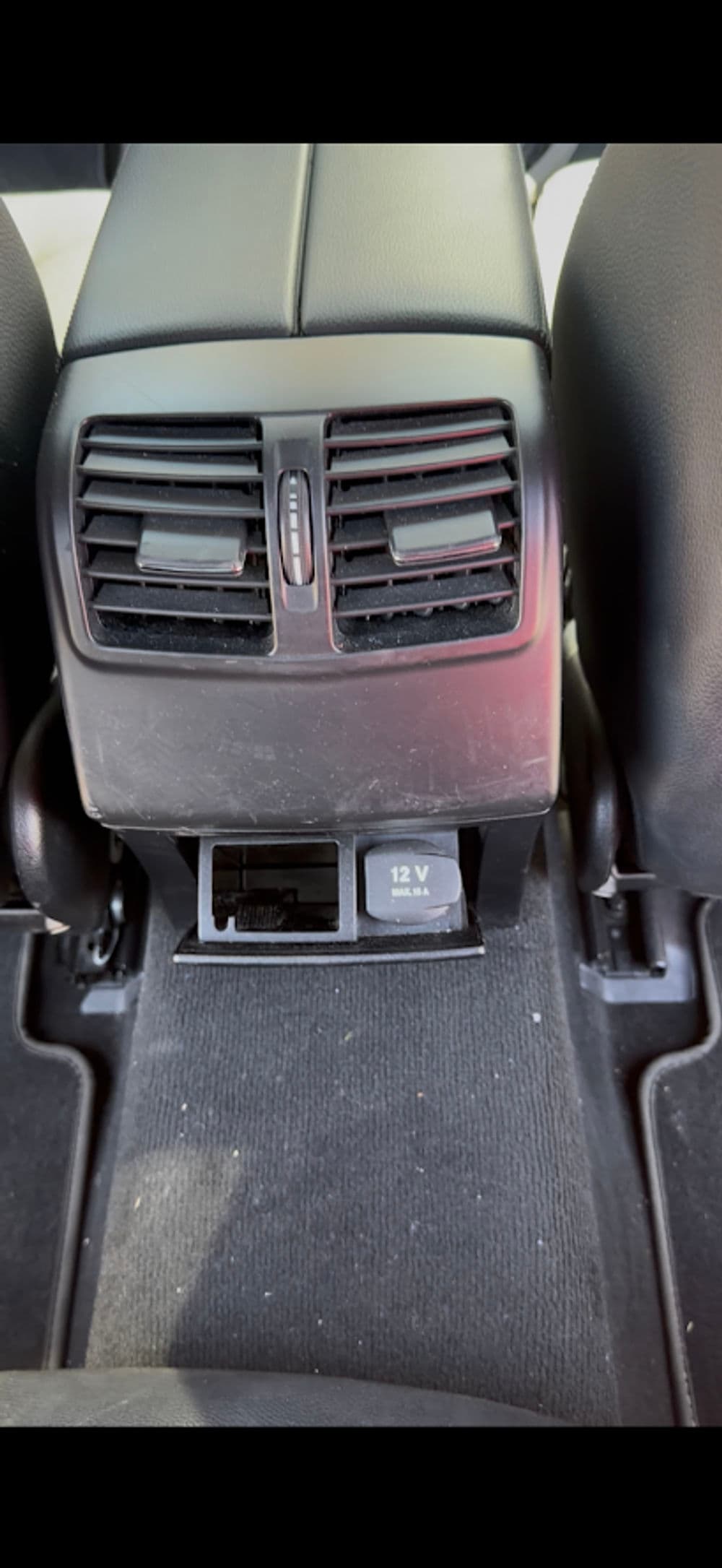 Car interior showing rear air vents and 12V charger socket on the center console floor.