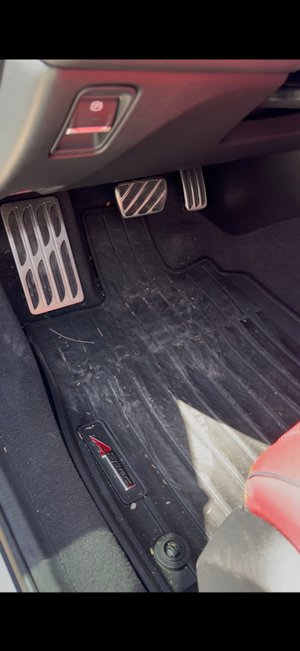 Car interior floor mats with dirt and pedals visible, featuring a red leather seat.